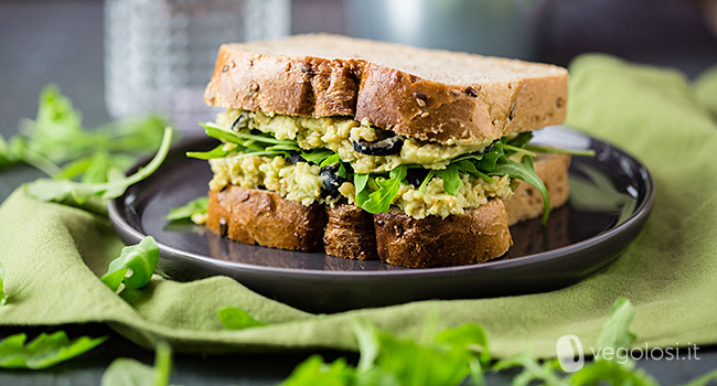 Sandwich ripieno di crema di ceci e avocado con olive e rucola