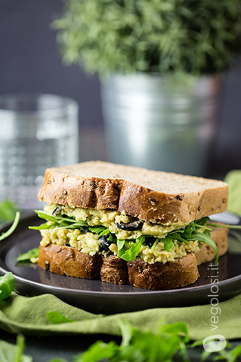 Sandwich ripieno di crema di ceci e avocado con olive e rucola